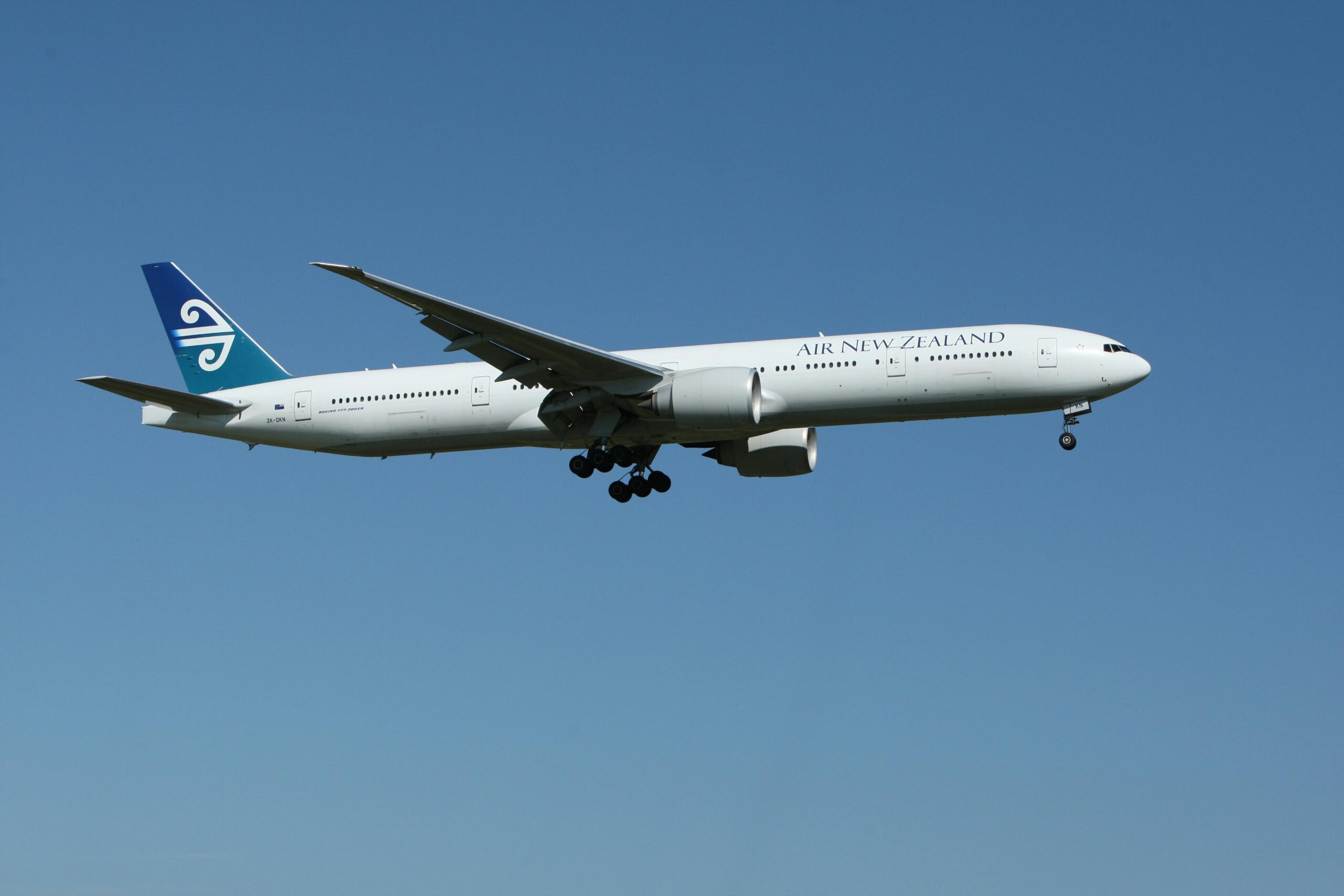 Air New Zealand Boeing 777 airliner flying against a clear blue sky, showcasing aviation travel.